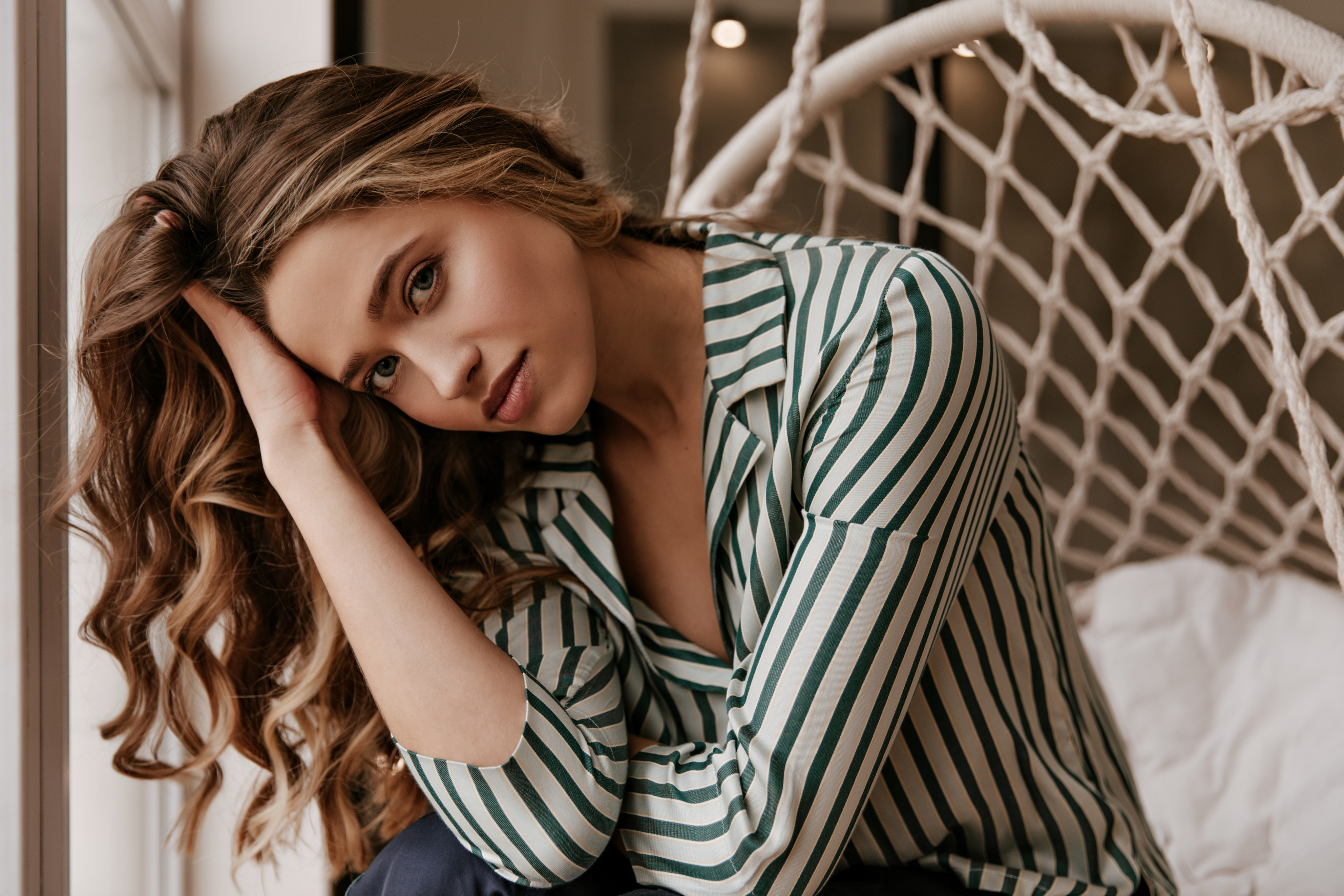 Woman with long, wavy highlighted hair relaxing in a woven hanging chair